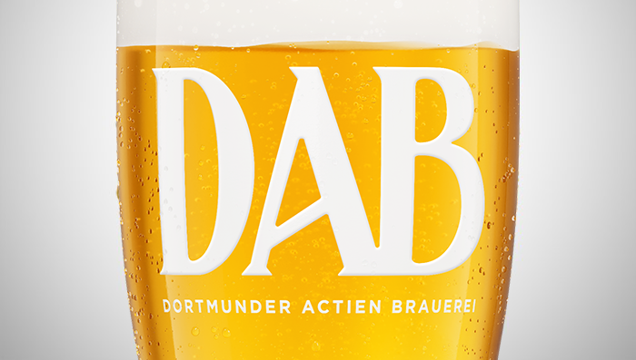 A close view of a beer glass filled with light golden beer and bubbles, featuring a large white logo.