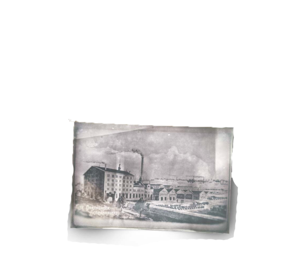 Une photo historique en noir et blanc représente un paysage industriel avec des bâtiments et des cheminées.
