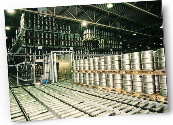 Un système de convoyage achemine des fûts de bière en métal dans une grande brasserie industrielle.