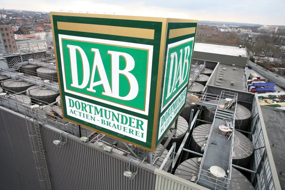 Large copper brewing vats stand in a spacious room with arched ceilings and ornate lamps.