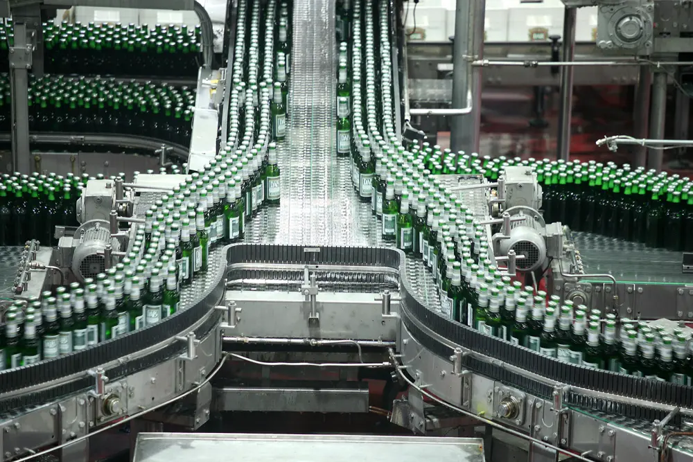 Un tapis roulant transporte de nombreuses bouteilles en verre vert dans un environnement d’usine.