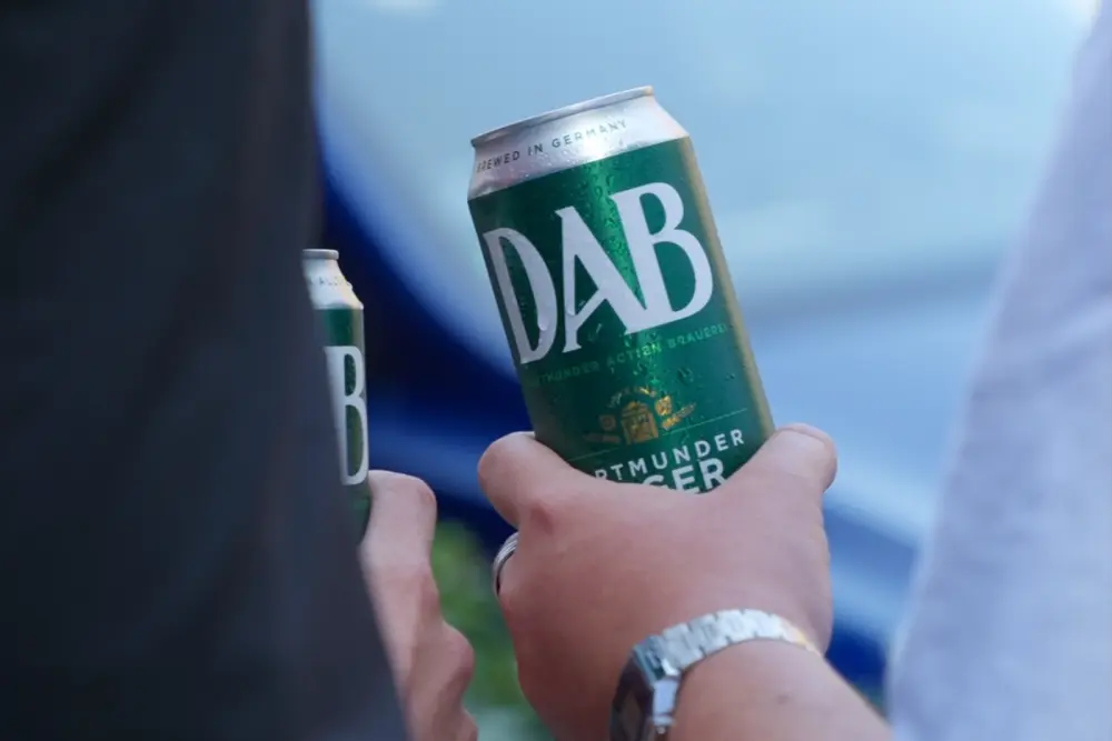Deux personnes tiennent chacune une canette de la marque DAB. L'une d'elles porte une montre et une bague.