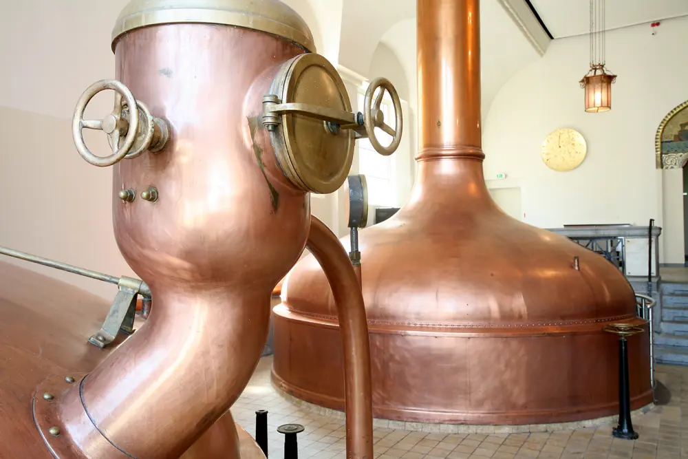 Une grande cuve de brassage en cuivre domine la pièce, équipée de valves et d'une surface polie.