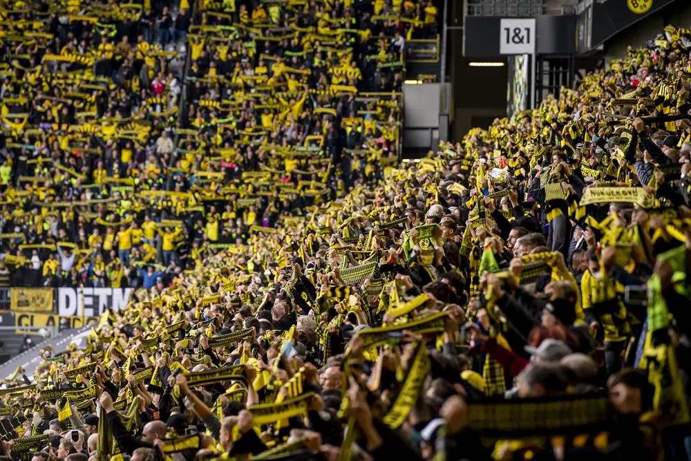 Une foule de fans enthousiastes en tenue jaune et noire acclame lors d’un événement sportif, remplissant les tribunes du stade.