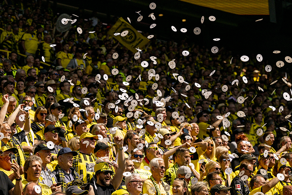 Une foule de supporters de football enthousiastes en jaune et noir célèbre en lançant des rouleaux de papier en l’air dans un stade.