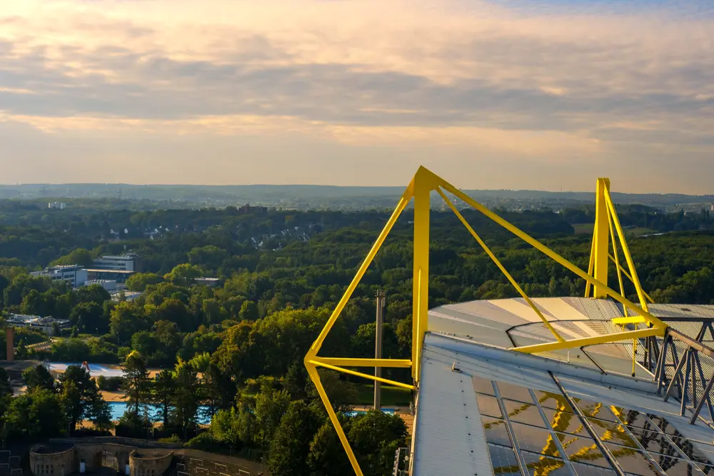 Une structure en acier jaune surmonte un bâtiment, dominant un paysage verdoyant sous un ciel nuageux.