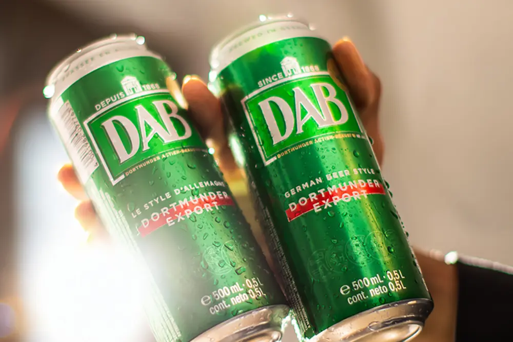 Deux mains tiennent des canettes de bière vertes et fraîches couvertes de condensation.